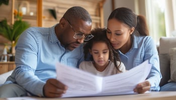 Close-knit family of three—a father, mother, and young daughter—sitting together and reviewing important documents in a cozy living room, symbolizing family planning and financial security.