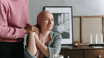 A woman wearing a headscarf sits thoughtfully while being comforted by someone holding her hand, symbolizing care, support, and resilience during challenging times.